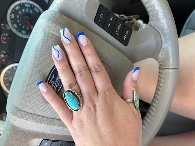 Hand with decorative nails on a car steering wheel